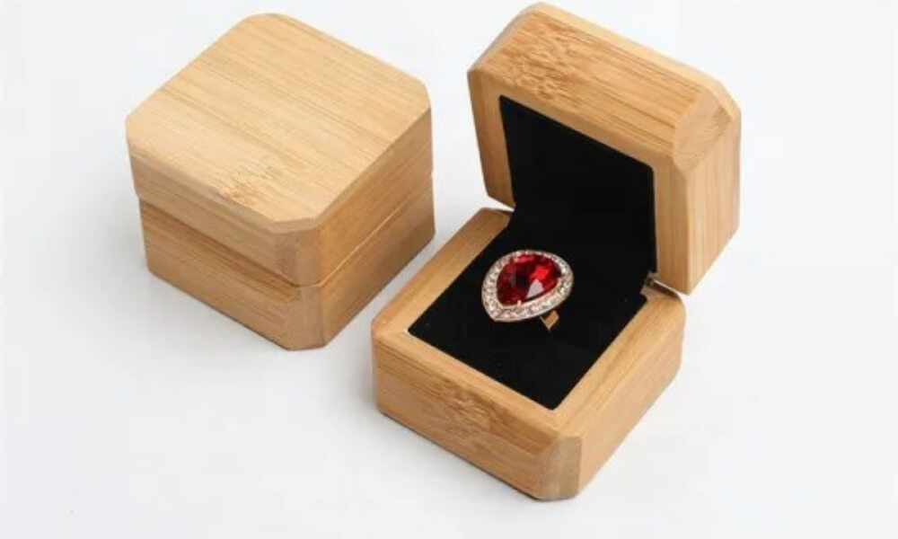A top view of a small square light-wood ring box sitting closed next to an open matching box displaying a ruby ring on black velvet